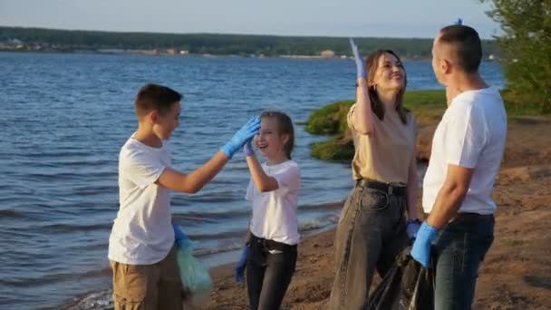 Familj på fyra med tonåringar som rensar stranden från plastskräp. Gemensamt arbete. Begreppet miljöutbildning — Stockvideo