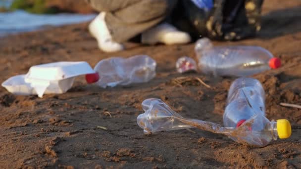 Eldivenli tanınmayan bir kadın nehir kenarındaki siyah bir pakette plastik şişe topluyor. — Stok video