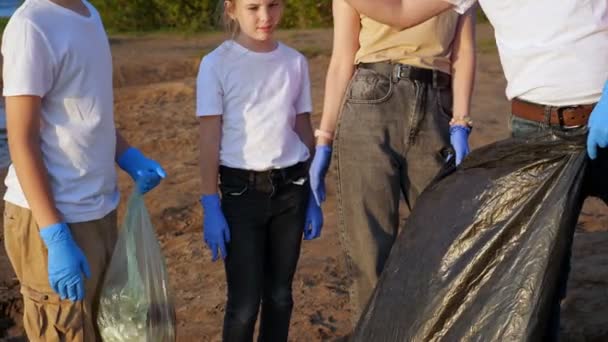 Groupe de quatre personnes avec un adolescent ramasser les ordures sur le rivage. Travail en commun. Concept d'éducation environnementale — Video