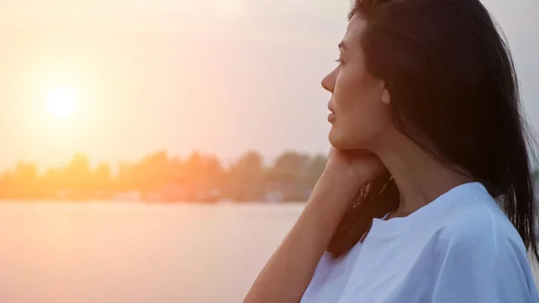 Jolie femme touche la joue contre la rivière tranquille au coucher du soleil — Photo