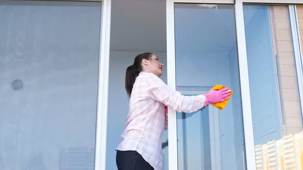 Bruneta žena v rukavicích se sprejem a hadrem myje okno, pohled zvenčí — Stock fotografie