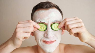 Yüzünde maske olan genç adam gözlerini kapatan salatalıkla oynuyor.