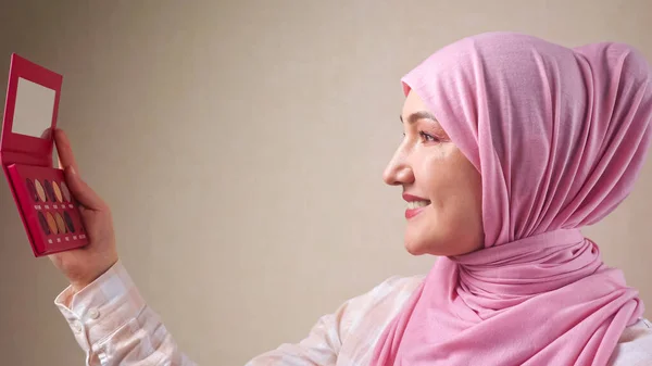 Giovane donna musulmana in hijab applicare il trucco con una spazzola guardando allo specchio — Foto Stock