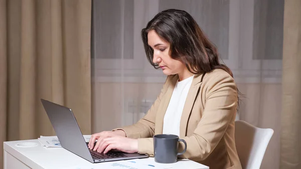 Молода жінка друкує руки на сірій клавіатурі ноутбука і дивиться на графіки — стокове фото