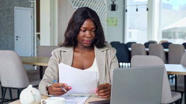 Siyahi iş kadını kafe 'de kağıt ve dizüstü bilgisayarla çalışıyor.