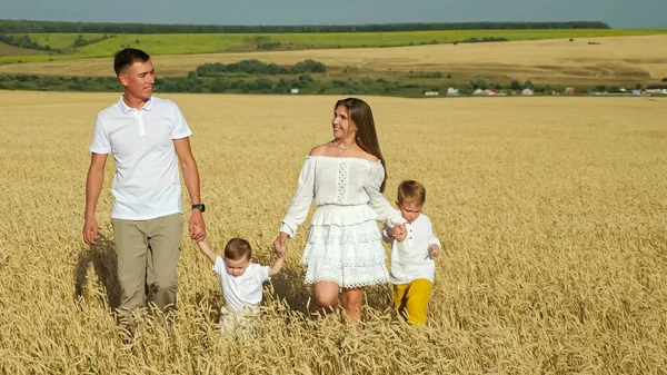 Família com crianças pequenas caminha no campo de trigo no verão — Fotografia de Stock