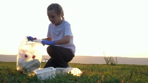 Teenage girl collects rubbish in gloves on the river bank — Stock Video