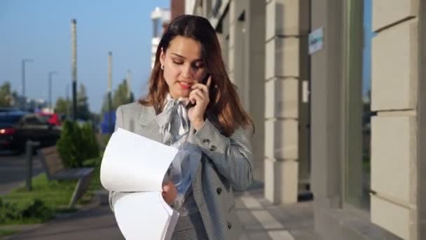 Ung kvinna i kostym är känslomässigt talar på telefonen och titta på de dokument som går ner på gatan — Stockvideo