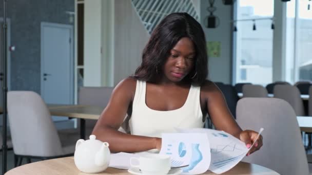 Mujer afroamericana trabaja con diagramas en la mesa en la cafetería — Vídeo de stock