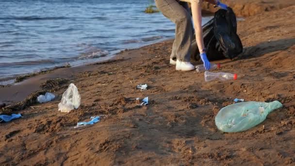 Mujer irreconocible en guantes recoge basura en una bolsa negra en la orilla del río — Vídeos de Stock