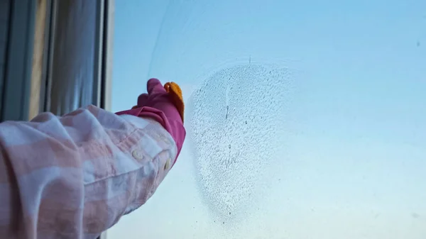 Gros plan des mains dans les gants nettoyant la fenêtre avec un chiffon sur fond de ciel clair — Photo