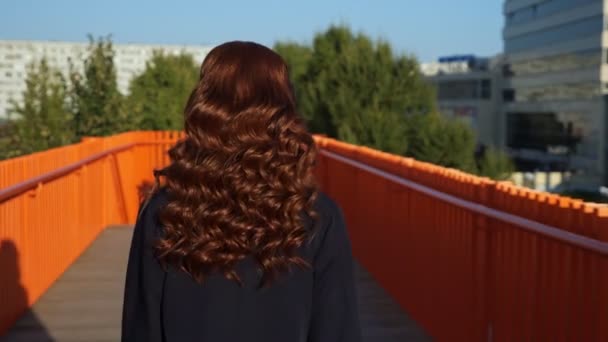 Señora con pelo de cobre camina girando hacia atrás a lo largo de pasarela — Vídeos de Stock