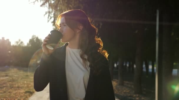 Pewna siebie młoda kobieta pije kawę spacerując wzdłuż drogi parku — Wideo stockowe