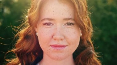 Kıvırcık saçlı çekici kadın kameraya gülümsüyor.