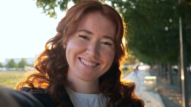 Frau mit lockigem roten Haar lässt Selfie im Stadtpark zwinkern — Stockvideo