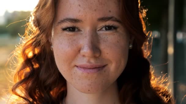 Молодая женщина с вьющимися медными волосами и веснушками в парке — стоковое видео