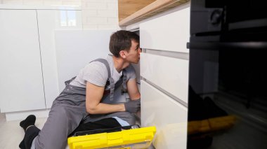 Gri tulumlu tesisatçının vidaları sökmesi için ingiliz anahtarı gerekir.