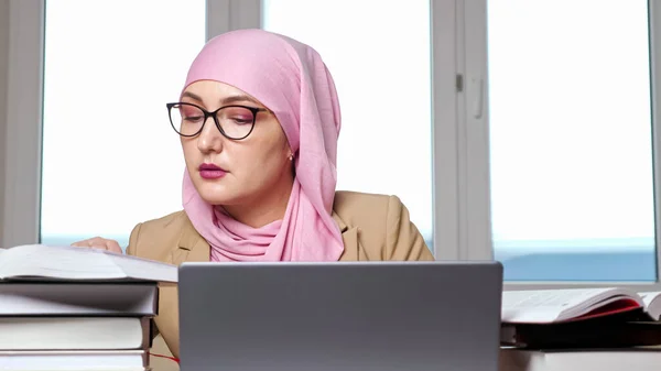Γυναίκα με μαντίλα και γυαλιά δακτυλογράφησης σε φορητό υπολογιστή που ψάχνει για βιβλία — Φωτογραφία Αρχείου