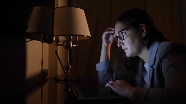 Karanlık bir akşamda takım elbiseli bir kadın dizüstü bilgisayarın başında oturuyor. — Stok video