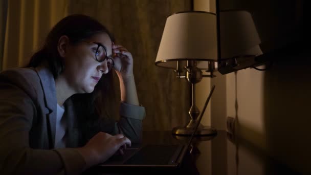 Woman in a business suit in a dark evening sits at a laptop, slow motion — Stock Video