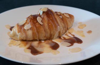 Ev yapımı kahvaltı için beyaz tabakta karamelli ve şuruplu kruvasan.