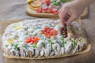 Cooking Focaccia. Raw focaccia creatively decorated with vegetables on parchment paper. Sourdough dough clipart