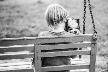 Bir çocuk salıncakta köpeğine sarılıyor.