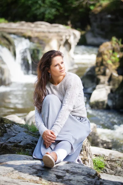 Güzel bir Bayan dikey çekim önünde bir şelale oturdu