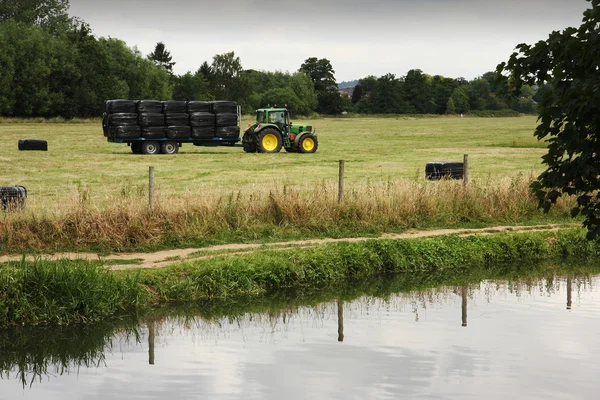 Tractor and trailer in field behind a canal Stock Image