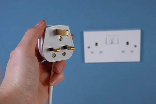 Hand holding a 3 pin plug with socket in the background Stock Image