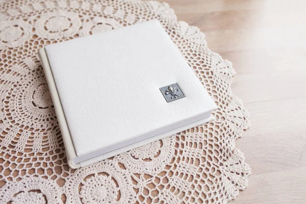 White photo book with leather cover. Stylish wedding photo album.  Family photoalbum on the white table . Beautiful notepad or photobook with elegant openwork embossing on a white background.
