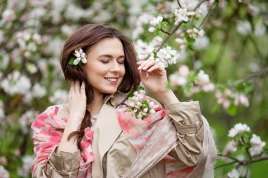 Bahar zamanı çiçek açan elma bahçesindeki güzel, gülümseyen esmer bir genç kadının portresi. Doğanın tadını çıkar. Sağlıklı bir kız. Bahar konsepti Meyve bahçesindeki güzel kız