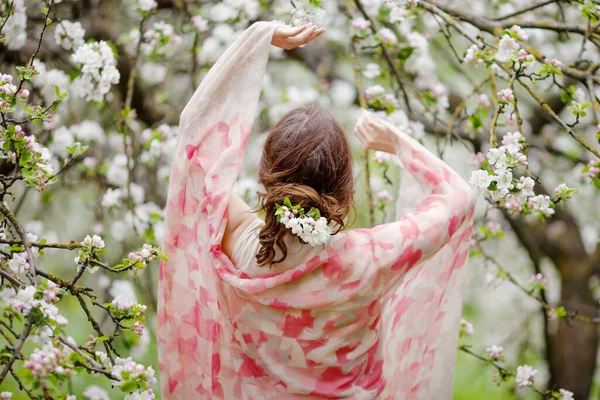 İlkbaharda çiçek açan elma bahçesinde güzel, gülümseyen esmer genç kadınlar. Doğanın tadını çıkar. Sağlıklı bir kız. Bahar konsepti Meyve bahçesindeki güzel kızın arka manzarası