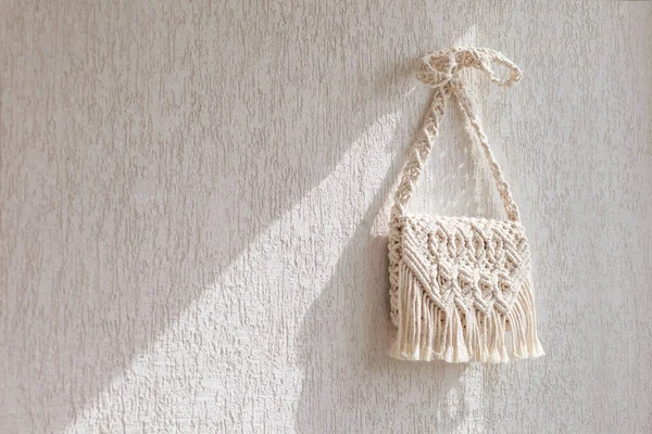 Handmade macrame bag  on the light wall. ECO friendly natural macrame cotton bag. Hobby knitting handmade macrame. Modern summer concept. Copy space