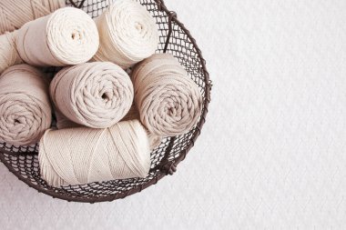 Beyaz arka planda el yapımı makrome örgü ve pamuk iplikler. Pamuk makrome kablolar ve ipler tel sepetine karşı. Makrome ve el sanatları afişleri ve reklam için iyi bir görüntü. Kapatın. Boşluğu kopyala