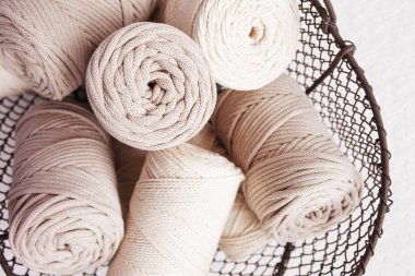 Beyaz arka planda el yapımı makrome örgü ve pamuk iplikler. Pamuk makrome kablolar ve tel sepetteki ipler. Kapat.