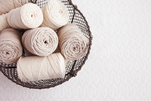 Beyaz arka planda el yapımı makrome örgü ve pamuk iplikler. Pamuk makrome kablolar ve ipler tel sepetine karşı. Makrome ve el sanatları afişleri ve reklam için iyi bir görüntü. Kapatın. Boşluğu kopyala