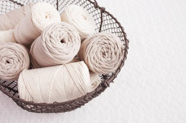 Beyaz arka planda el yapımı makrome örgü ve pamuk iplikler. Pamuk makrome kablolar ve ipler tel sepetine karşı. Makrome ve el sanatları afişleri ve reklam için iyi bir görüntü. Kapatın. Boşluğu kopyala