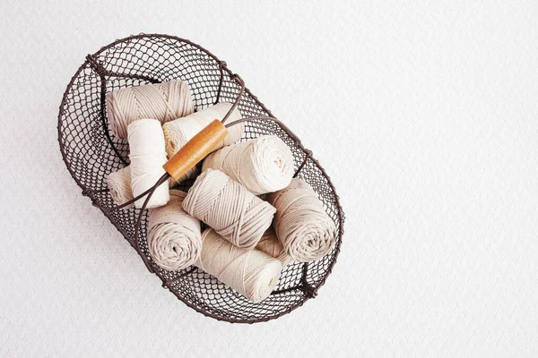 Beyaz arka planda el yapımı makrome örgü ve pamuk iplikler. Pamuk makrome kablolar ve ipler tel sepetine karşı. Makrome ve el sanatları afişleri ve reklam için iyi bir görüntü. Kapatın. Boşluğu kopyala