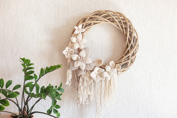 Macrame wreath with big cotton flower on a white decorative plaster wall. Natural cotton thread and rope. Eco decor for home. Creative greeting card for a creative person.