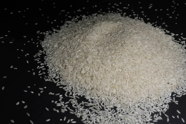 Arroz branco não cozido espalhado em cereais sobre um fundo preto — Fotografia de Stock