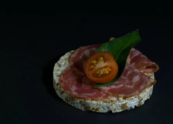 Pane croccante di riso croccante pane dietetico e panino affumicato alla salsiccia con mezzo pomodoro ciliegia. Torta di riso riso soffiato con salame, salsiccia, balyk, carne affumicata su fondo nero — Foto Stock