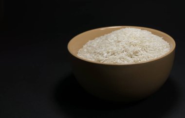 Beyaz pişmemiş pirinç, siyah arka planda dağınık taneciklerle dolu bir kasede.