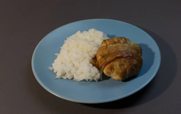 用咸肉包裹的鸡排包在灰色背景的蓝色盘子里的煮沸的白饭 烤鸡肉肉丸配饰 — 图库照片