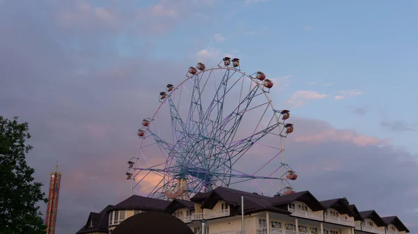 Rueda Ferris de colores brillantes contra el cielo del atardecer. Lazarevskoye, Sochi, Rusia, En la rueda la inscripción Lazarevskoe — Foto de Stock