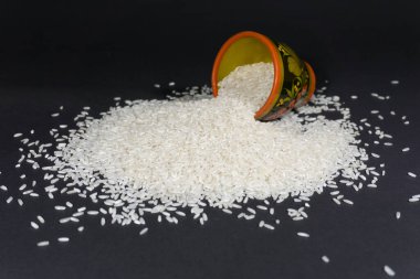 Fırınlanmamış pirinç taneleri ve siyah arka planda boyanmış ahşap bardak.