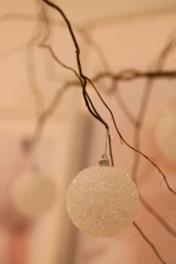 Ilık bir atmosferde ince, kıvrımlı dallardan sarkan beyaz parıltılı süsler yumuşak ışığı yakalıyor ve mevsim için neşeli bir hava yaratıyor..