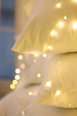 Üç yumuşak yastık birbirine yaslanmış, yavaşça parıldayan sıcak peri ışıklarıyla aydınlatılıyor. Huzur ortamı rahatlamak için rahat ve davetkar bir ortam yaratır..