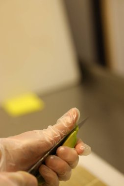 Bıçak tutan eldiven takan bir ele yakından bakmak. Mutfakta yeşil bir sebze kesiyor. Bu, ilkbaharda bir Paskalya yemeği hazırlama sırasında olur..