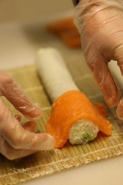 Bir aşçı Paskalya kutlaması sırasında bambu hasırına baharatlı pirinç sararak suşi hazırlar. Elleri hijyen için eldivenlerle kaplı..